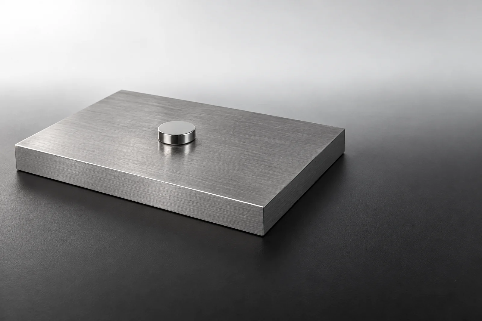 A nickel-plated neodymium disc magnet held flat against a thick mild steel plate